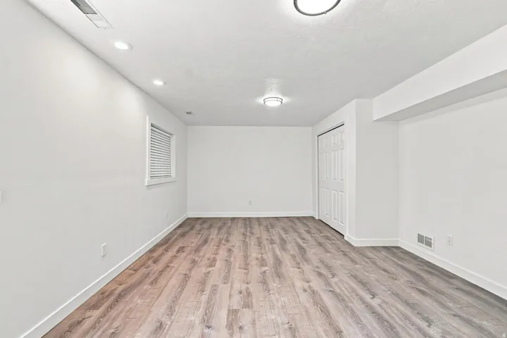Recessed lighting and a flush mount fixture illuminate this room with wood-finish flooring