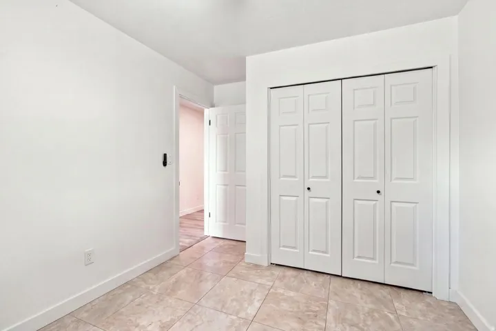 Neutral-toned tile flooring, white walls, and bi-fold closet doors with black hardware