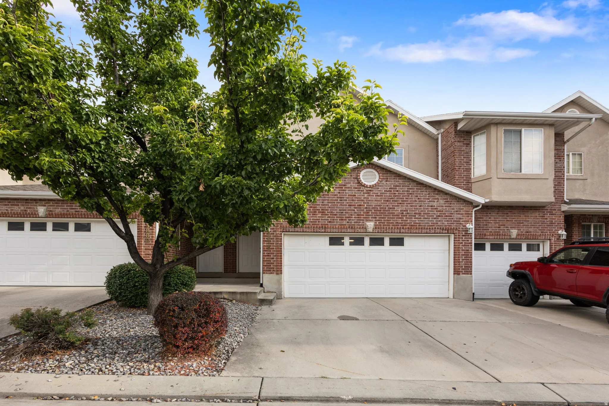 Brick facade with a bay window, white garage doors, and mature landscaping