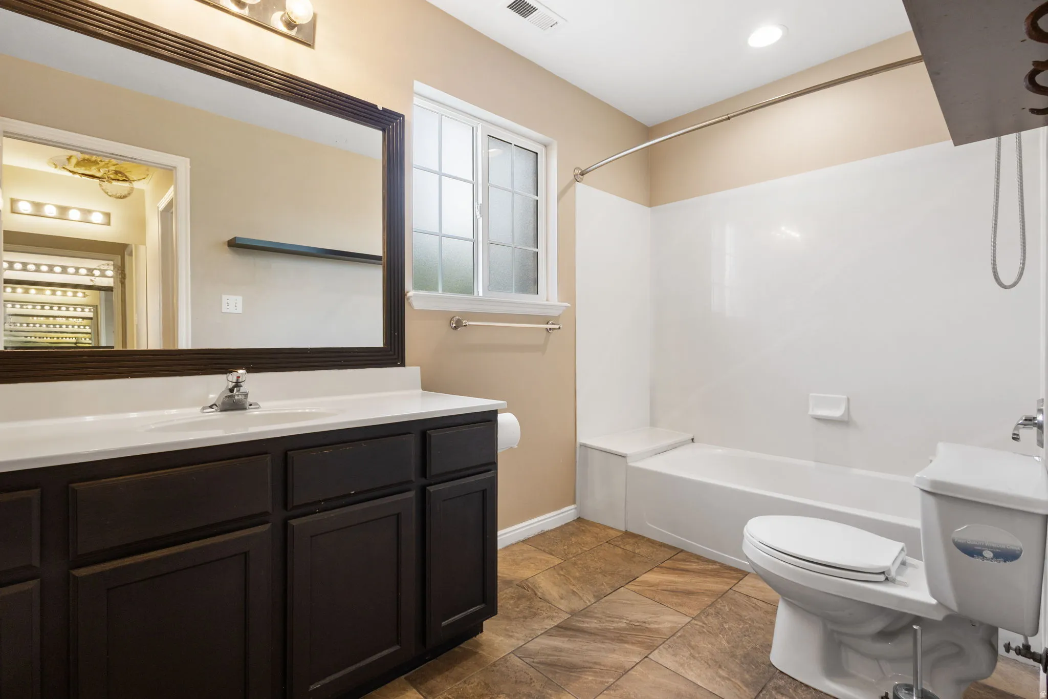 Master bathroom featuring a dark wood vanity with dual sinks, white quartz countertop, large framed mirror with integrated lighting, and ceramic tile flooring