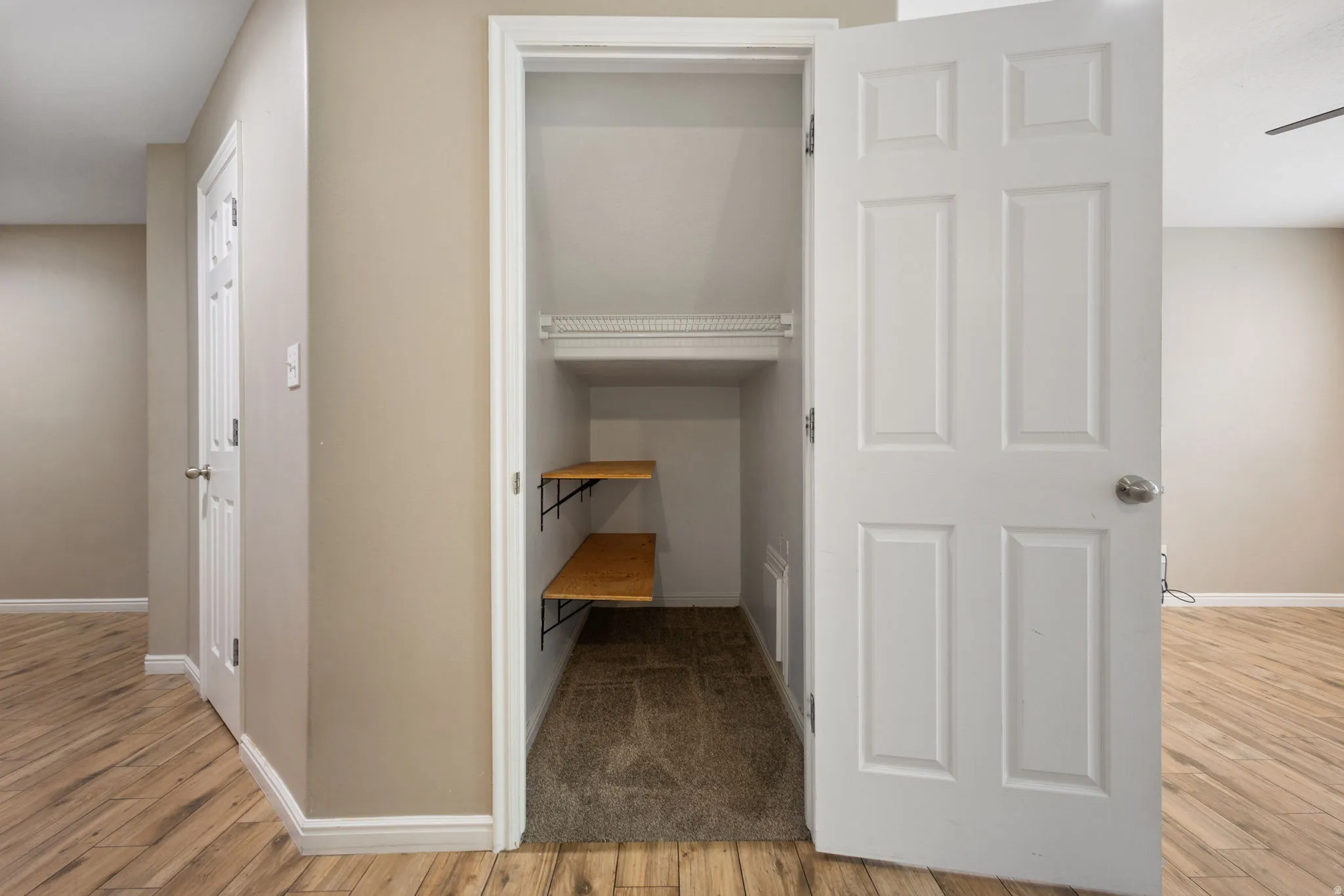 Recessed closet with wire shelving and two wood-finish shelves, carpeted floor