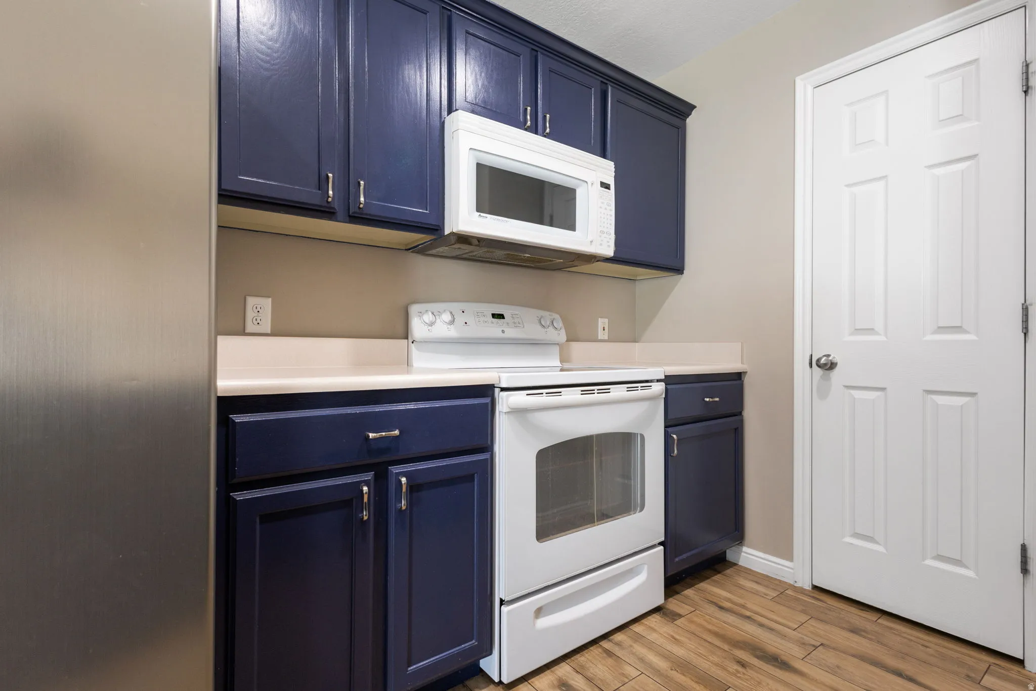 Kitchen featuring dark blue cabinetry, light-toned countertops, wood-finish flooring, and white appliances
