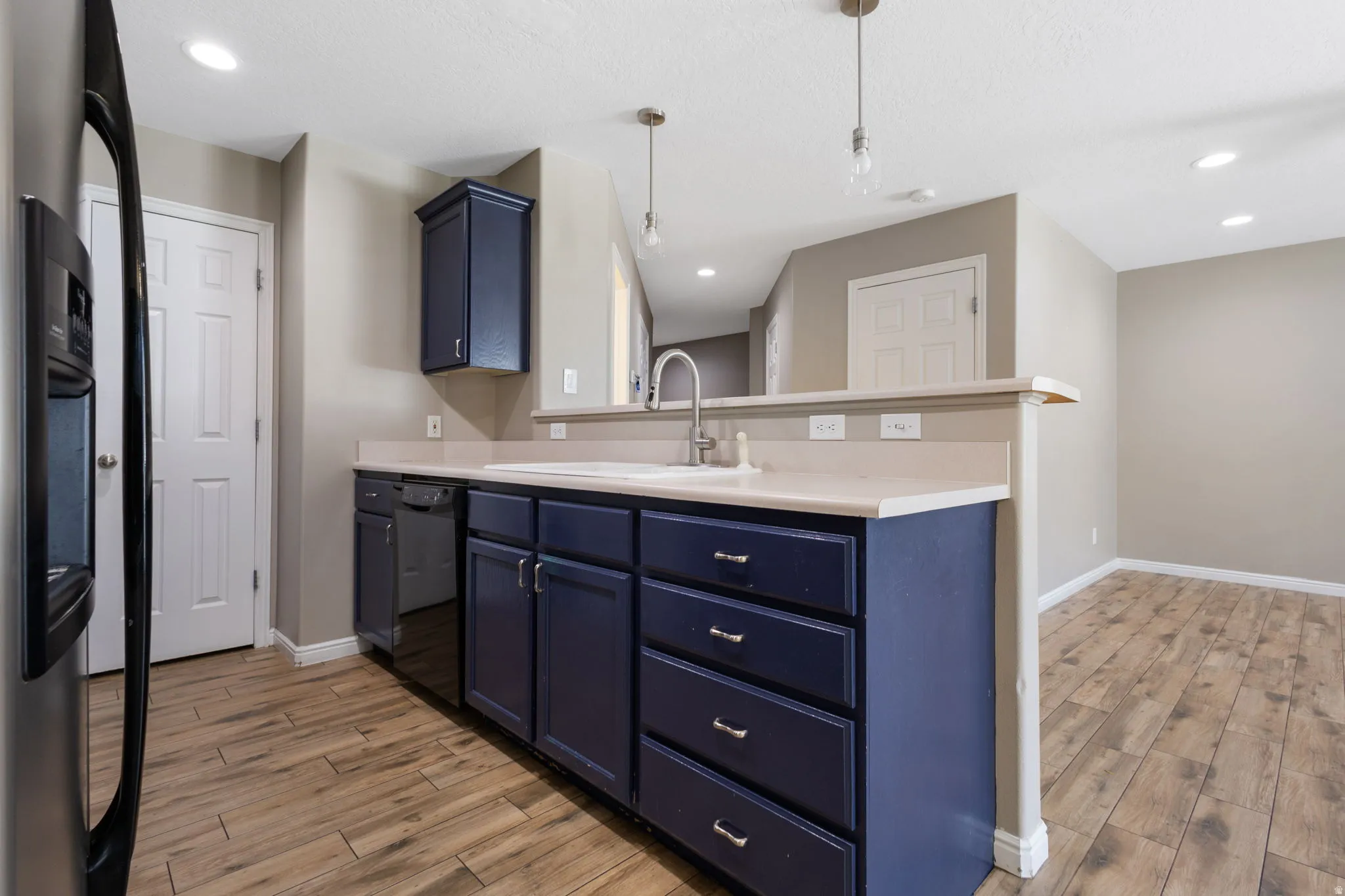 Kitchen featuring wood-finish flooring, dark blue cabinetry, a stainless steel refrigerator, and a built-in dishwasher