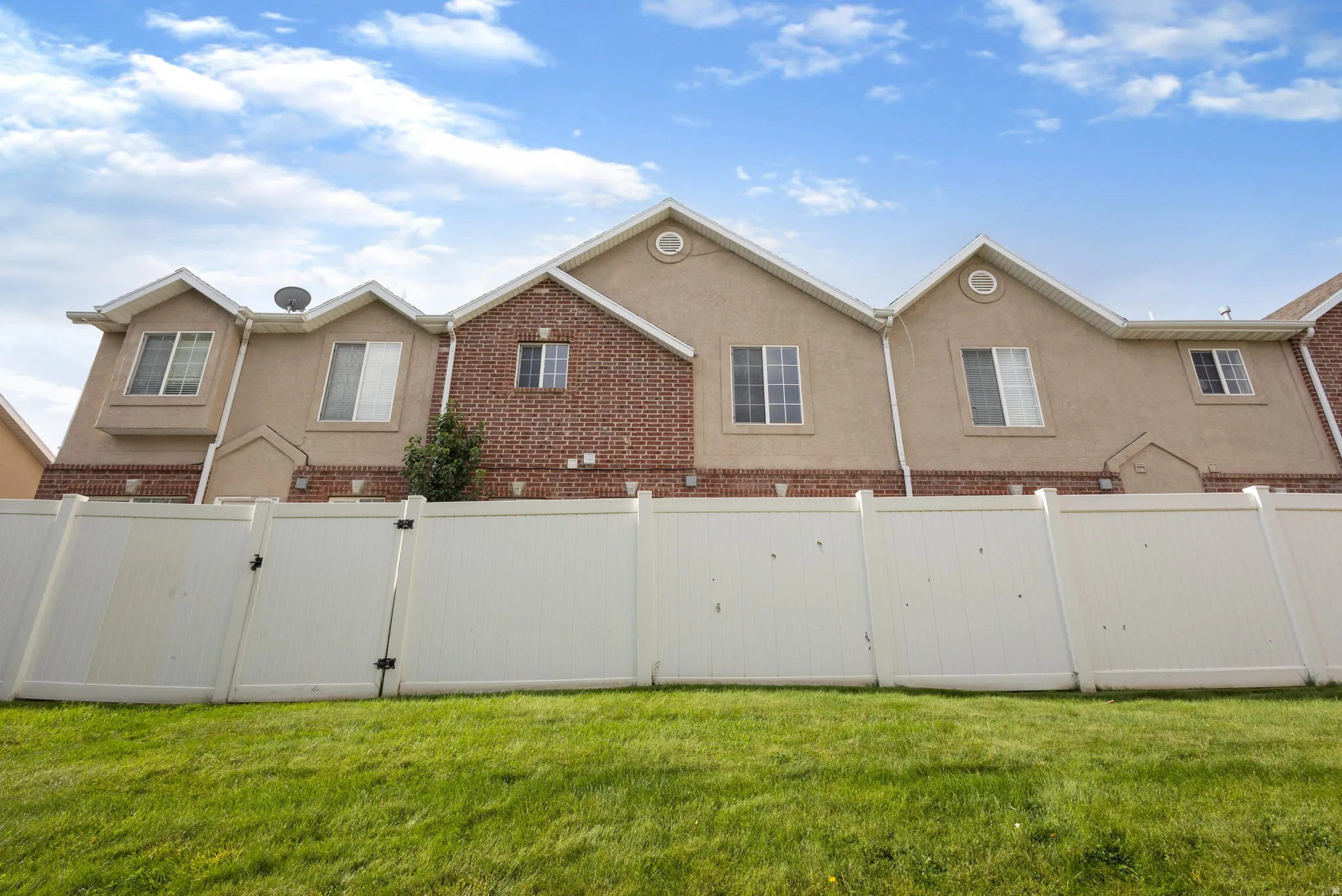 Exterior elevation featuring stucco and brick finishes, multiple windows, and a white privacy fence