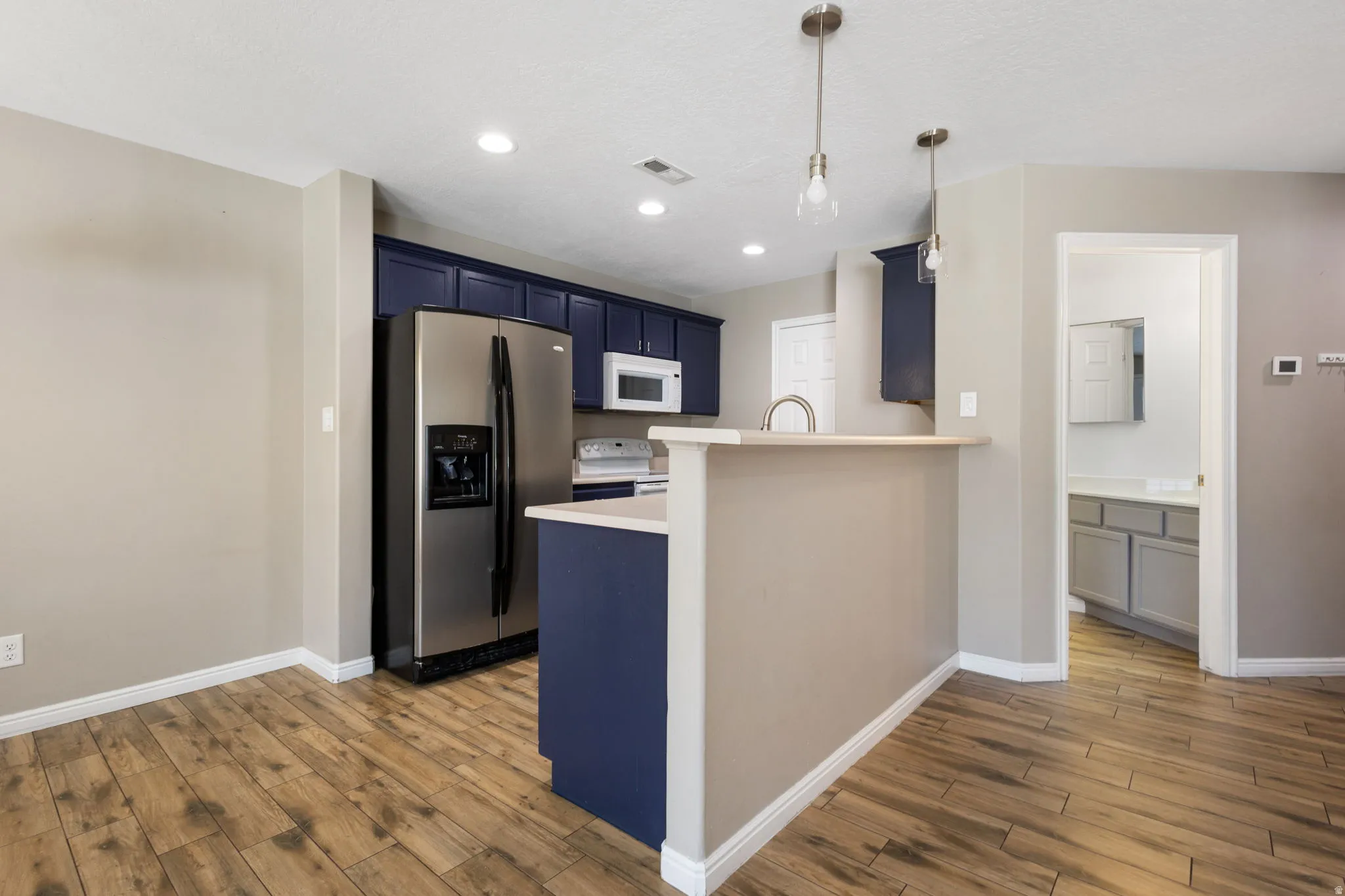 Wood-finish flooring, recessed lighting, stainless steel appliances, dark blue cabinetry, and a kitchen island with a breakfast bar