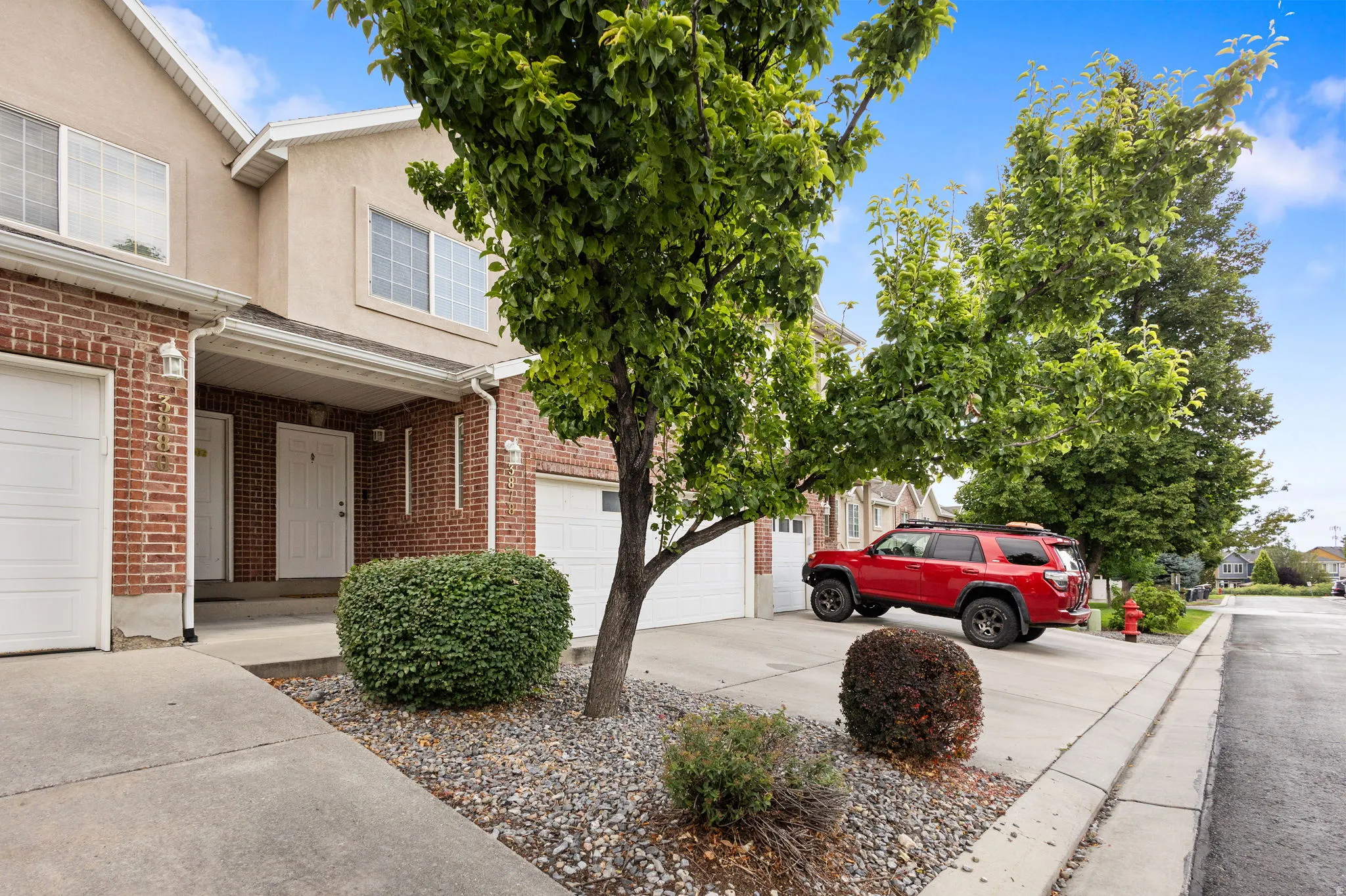 Brick and stucco exterior with multiple windows, attached garage, and mature landscaping