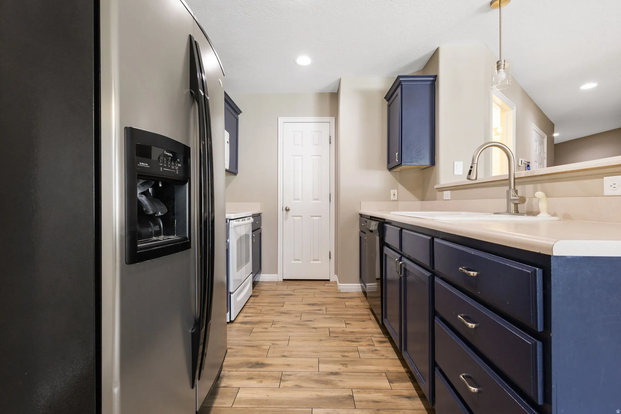 Kitchen with wood-finish flooring, dark blue cabinetry, light-toned countertops, and stainless steel appliances