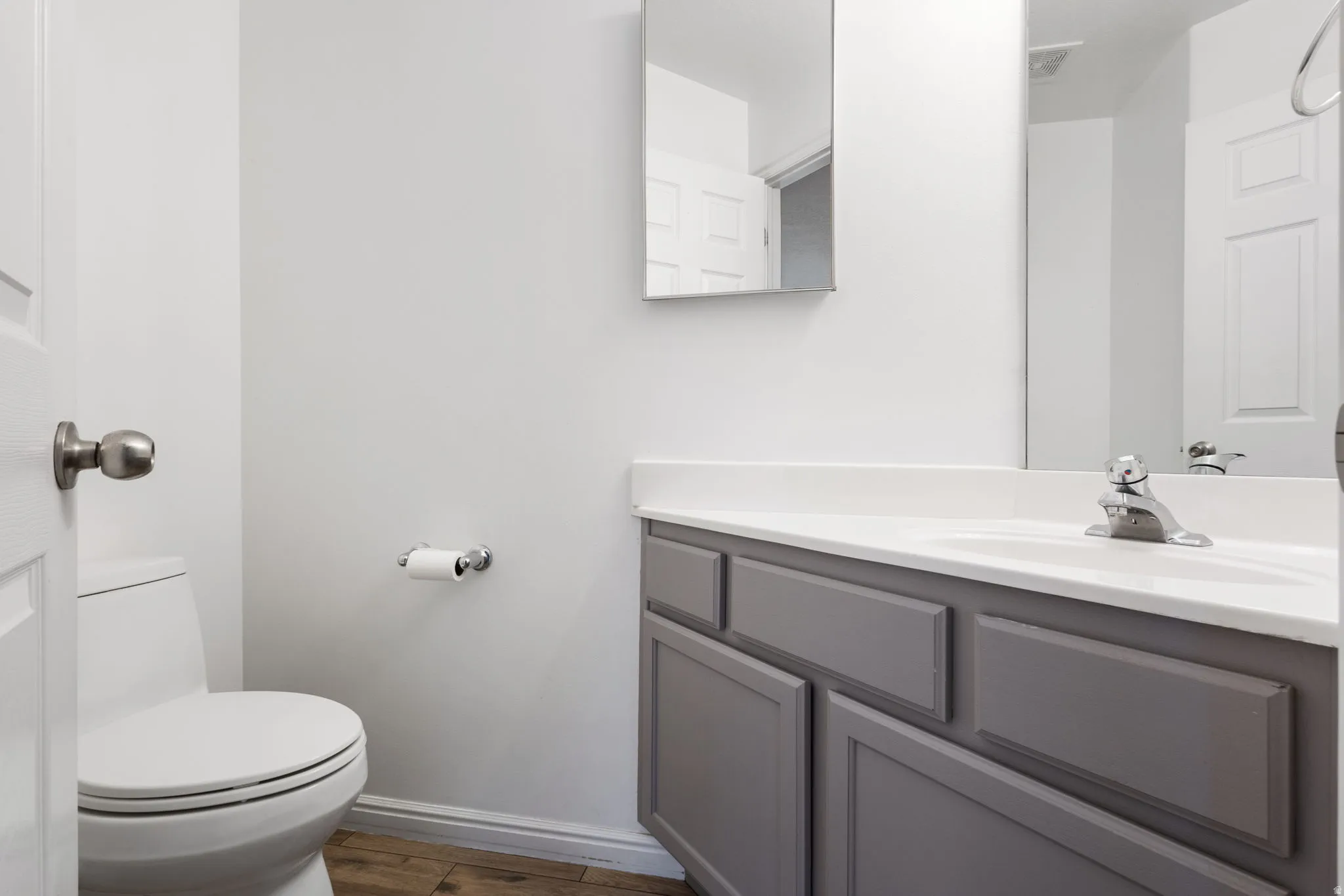 Gray vanity with a white countertop and integrated sink, chrome faucet, and mirrored medicine cabinet