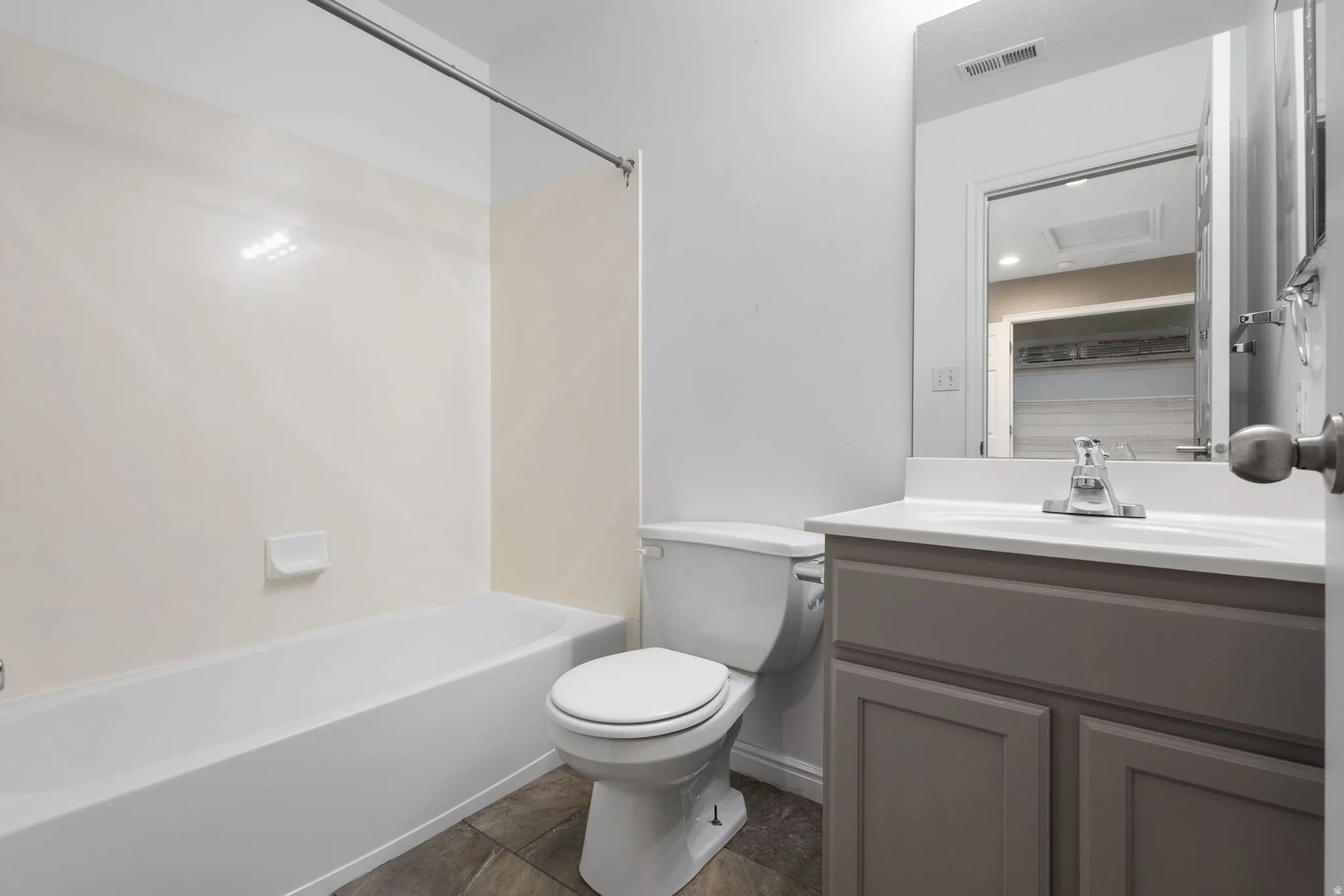 White bathtub and shower surround, toilet, gray vanity with white countertop, and wall-mounted mirror
