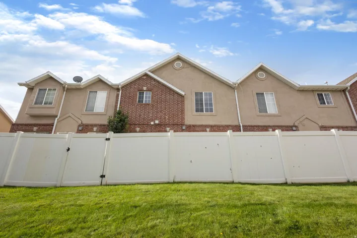 Exterior elevation featuring stucco and brick finishes, multiple windows, and a white privacy fence