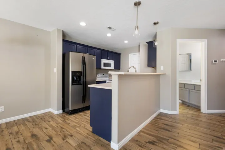 Wood-finish flooring, recessed lighting, stainless steel appliances, dark blue cabinetry, and a kitchen island with a breakfast bar