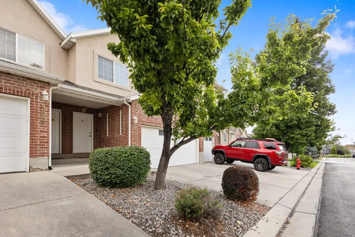 Brick and stucco exterior with multiple windows, attached garage, and mature landscaping