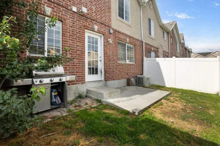 Brick exterior with a glass-paned door, concrete patio, and a white privacy fence