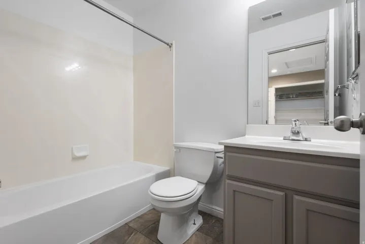 White bathtub and shower surround, toilet, gray vanity with white countertop, and wall-mounted mirror