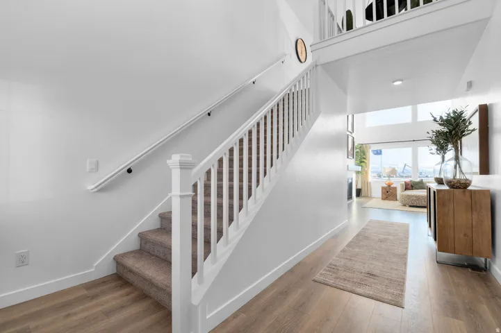 Carpeted staircase with white balusters, wood-finish flooring, and high ceilings
