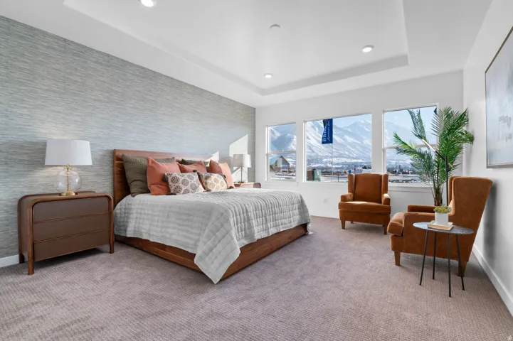 Textured accent wall, recessed lighting, tray ceiling, large windows, and neutral carpet flooring