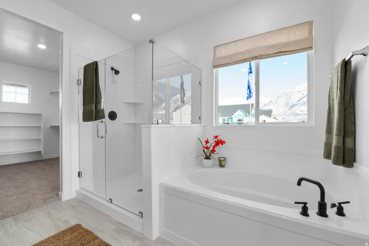 Soaking tub with matte black fixtures, glass-enclosed shower, white tile-finish flooring, recessed lighting, and a neutral-toned window treatment