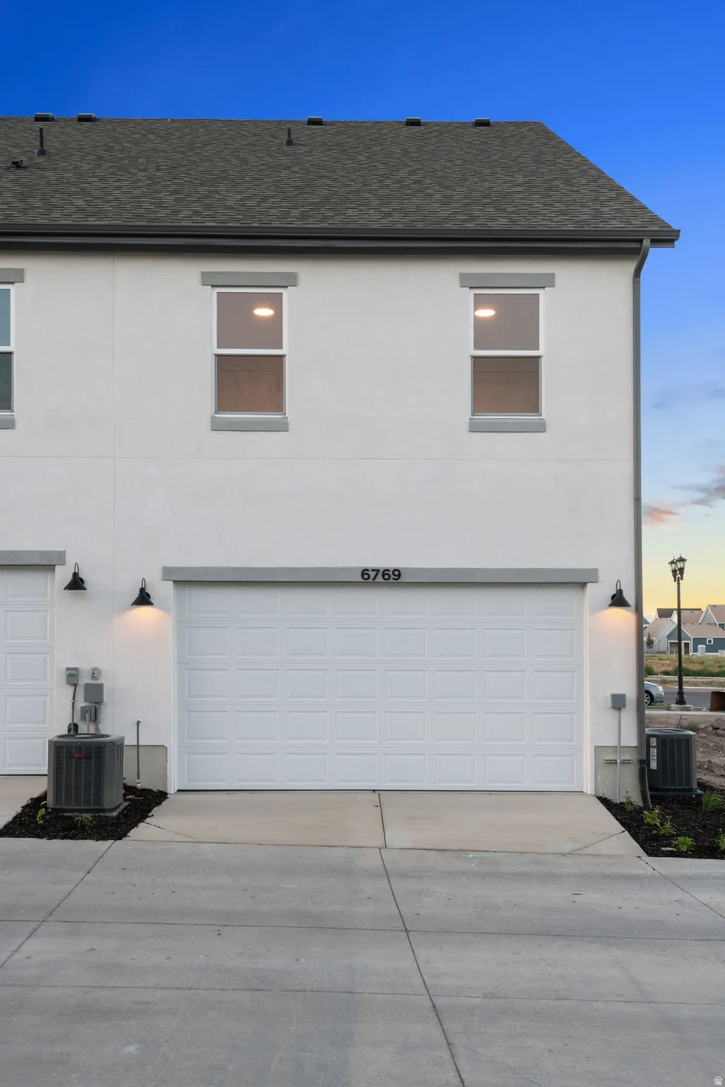 Stucco exterior with a pitched shingle roof, two upper-level windows, and a panel garage door with overhead numbering