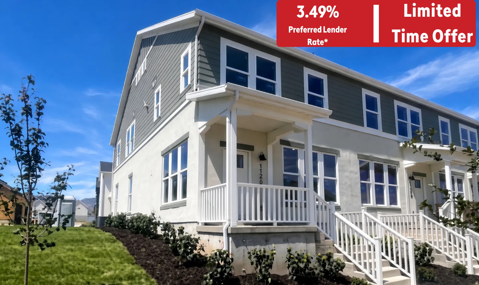 Modern townhome exterior featuring a white stucco finish, contrasting dark siding, multiple windows, a covered porch with white railings, and manicured landscaping