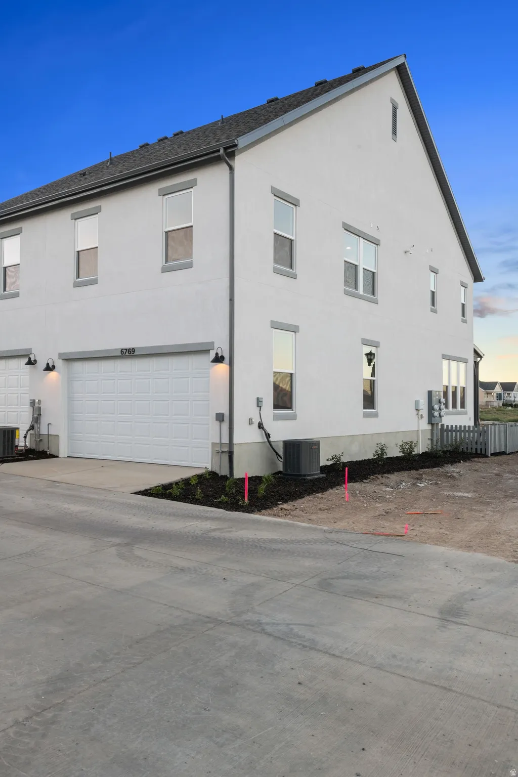 White stucco exterior with gray trim, attached garage with white door, and dark shingle roof