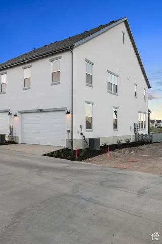 White stucco exterior with gray trim, attached garage with white door, and dark shingle roof