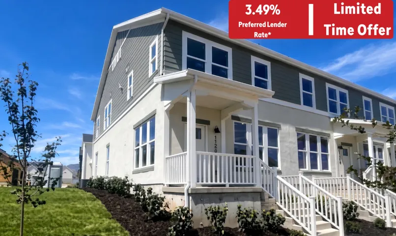 Modern townhome exterior featuring a white stucco finish, contrasting dark siding, multiple windows, a covered porch with white railings, and manicured landscaping