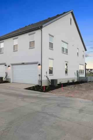 White stucco exterior with gray trim, attached garage with white door, and dark shingle roof