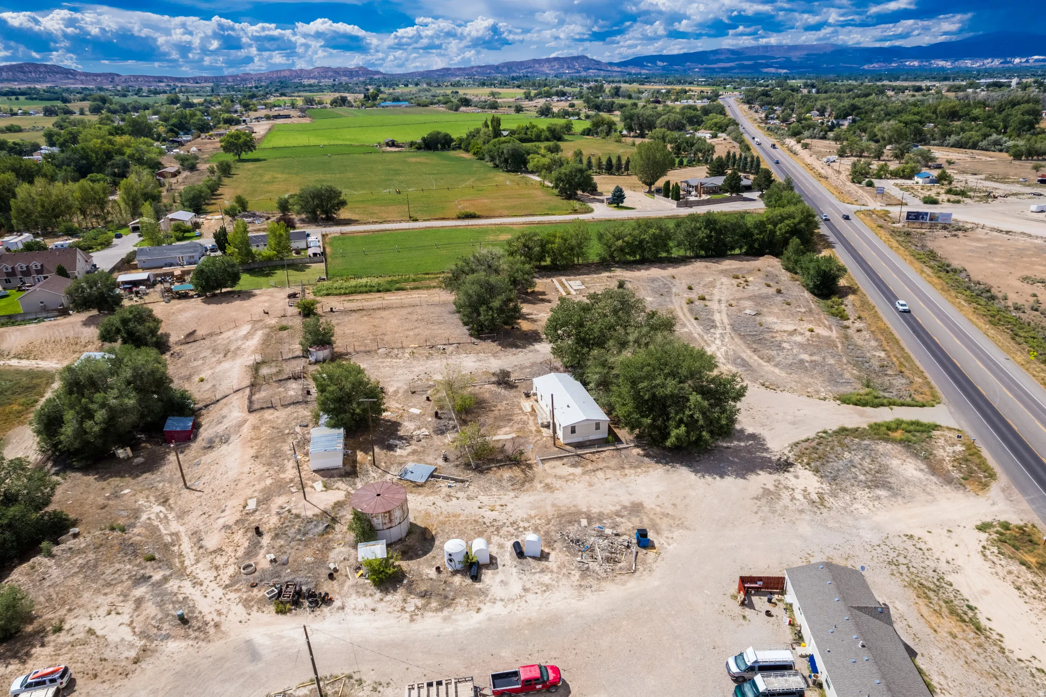 Expansive land featuring a single-story structure, multiple mature trees, and direct road frontage