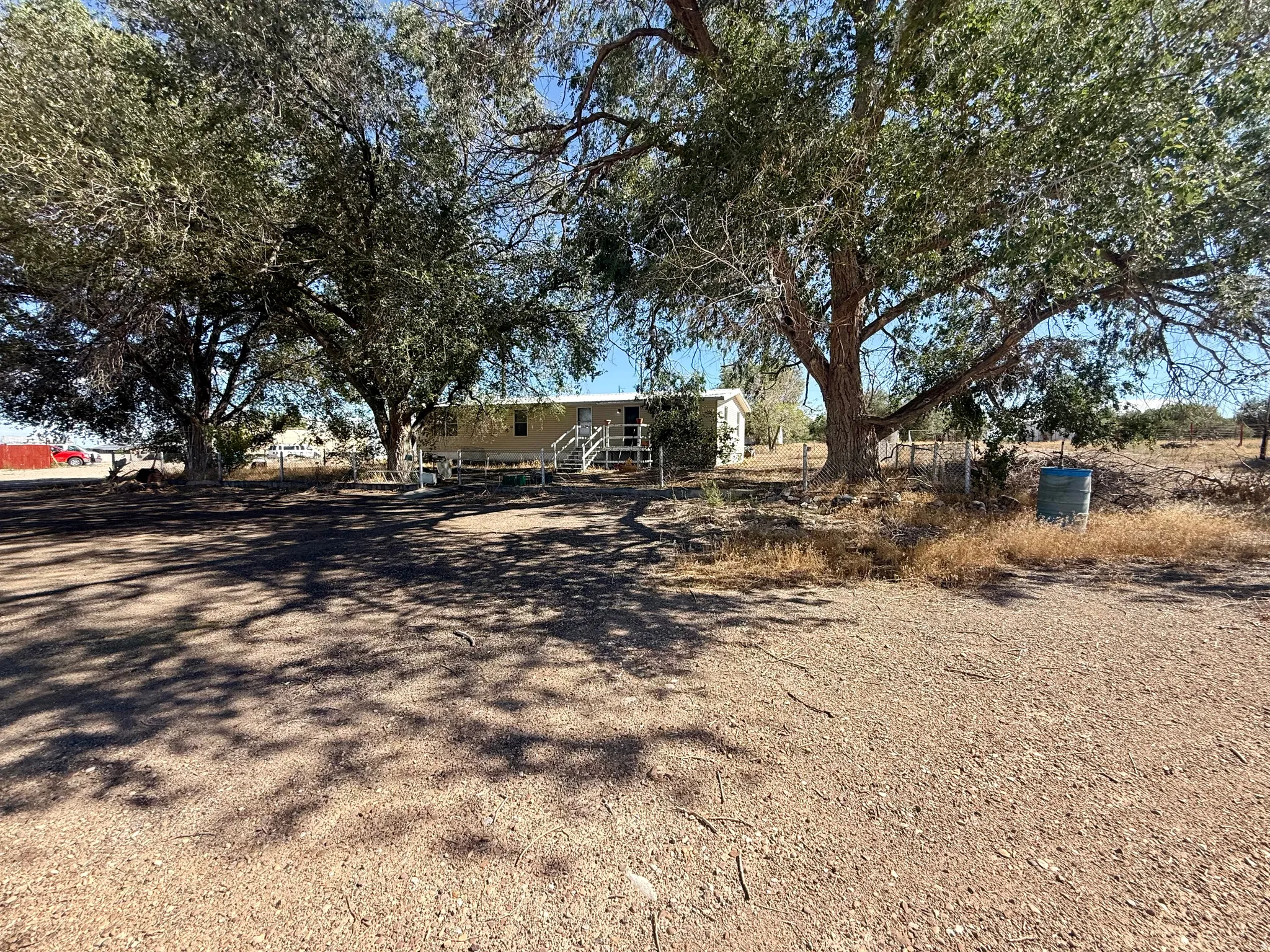 Expansive dirt lot featuring mature trees and a residential structure with an elevated porch