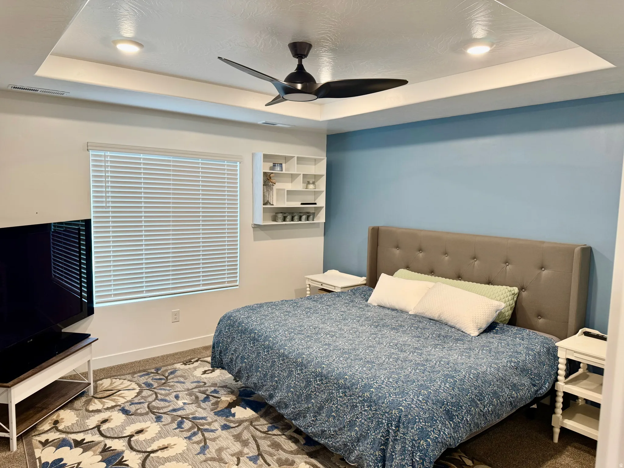 Tray ceiling with recessed lighting, ceiling fan, window with blinds, and built-in shelving