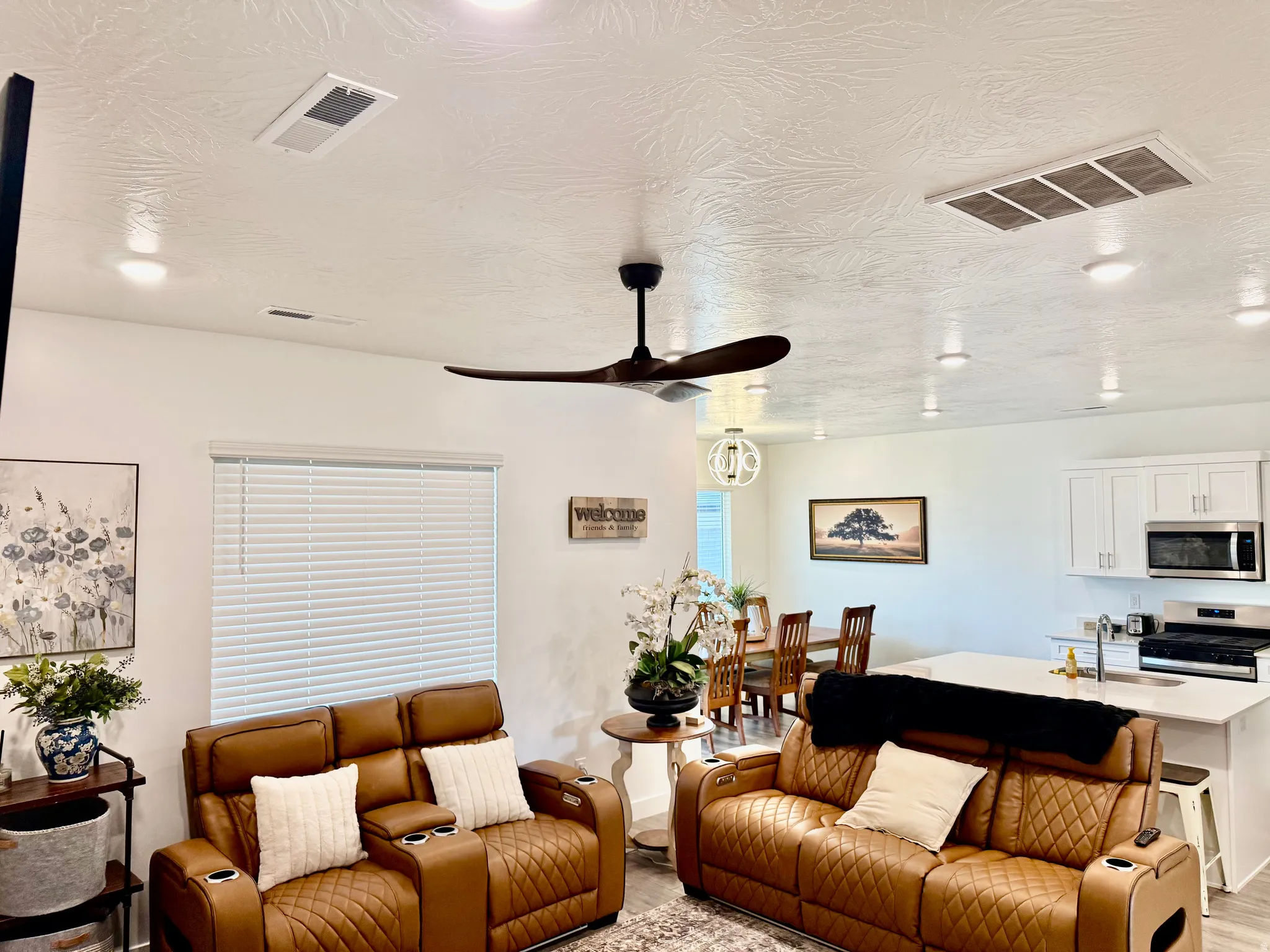 Recessed lighting throughout, ceiling fan with dark wood-finish blades, window with blinds, white kitchen cabinetry, stainless steel kitchen appliances