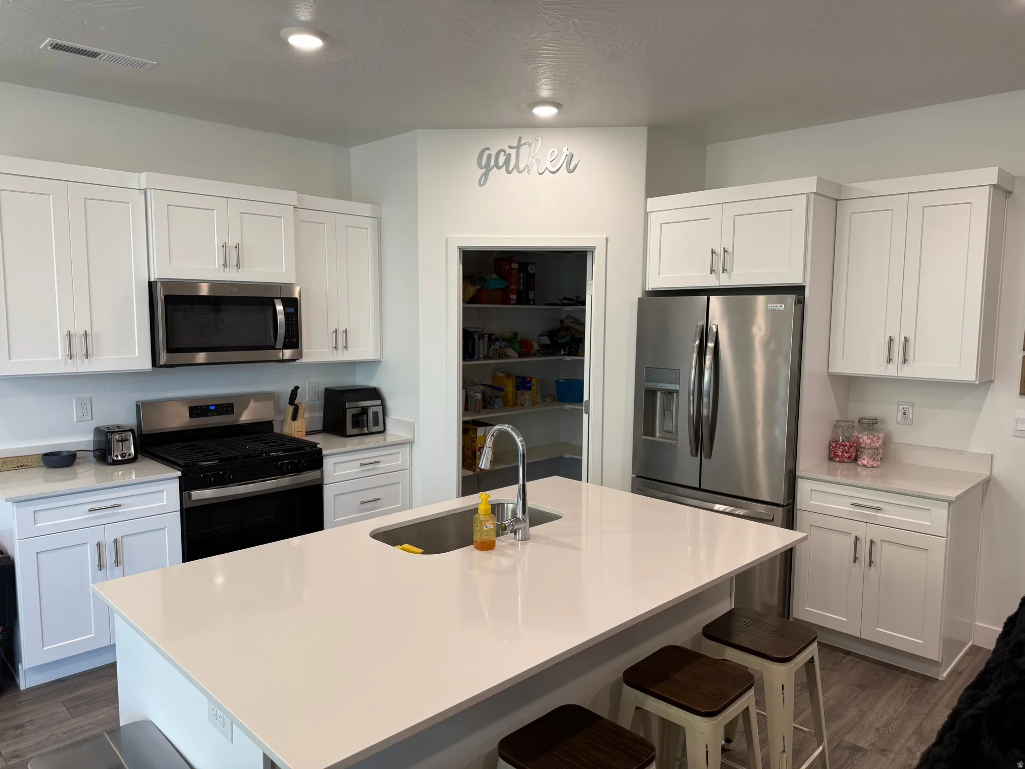 Modern kitchen featuring white cabinetry, stainless steel appliances, a center island with an undermount sink, and light-toned countertops