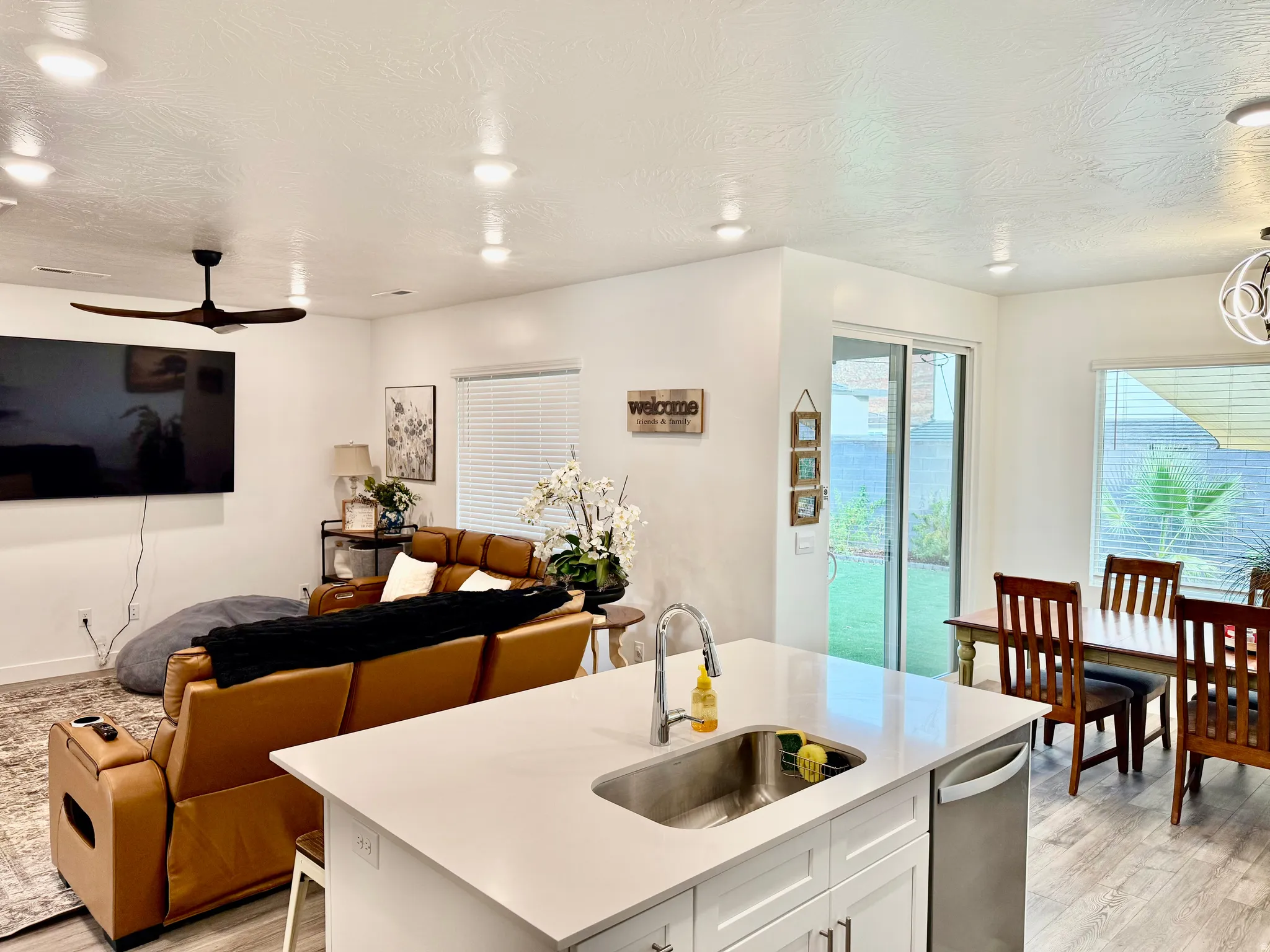 Open-concept living area featuring a kitchen island with sink, stainless steel dishwasher, sliding glass door access to the outdoor space, and wood-finish flooring