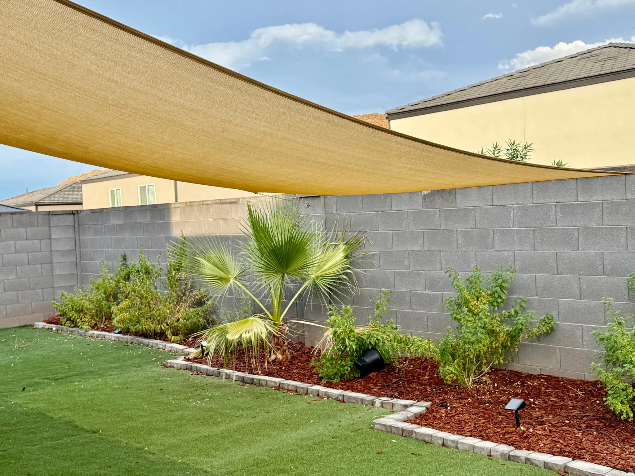 Expansive backyard featuring artificial turf, a shade sail, and landscaped planting beds with decorative wood chips and assorted foliage