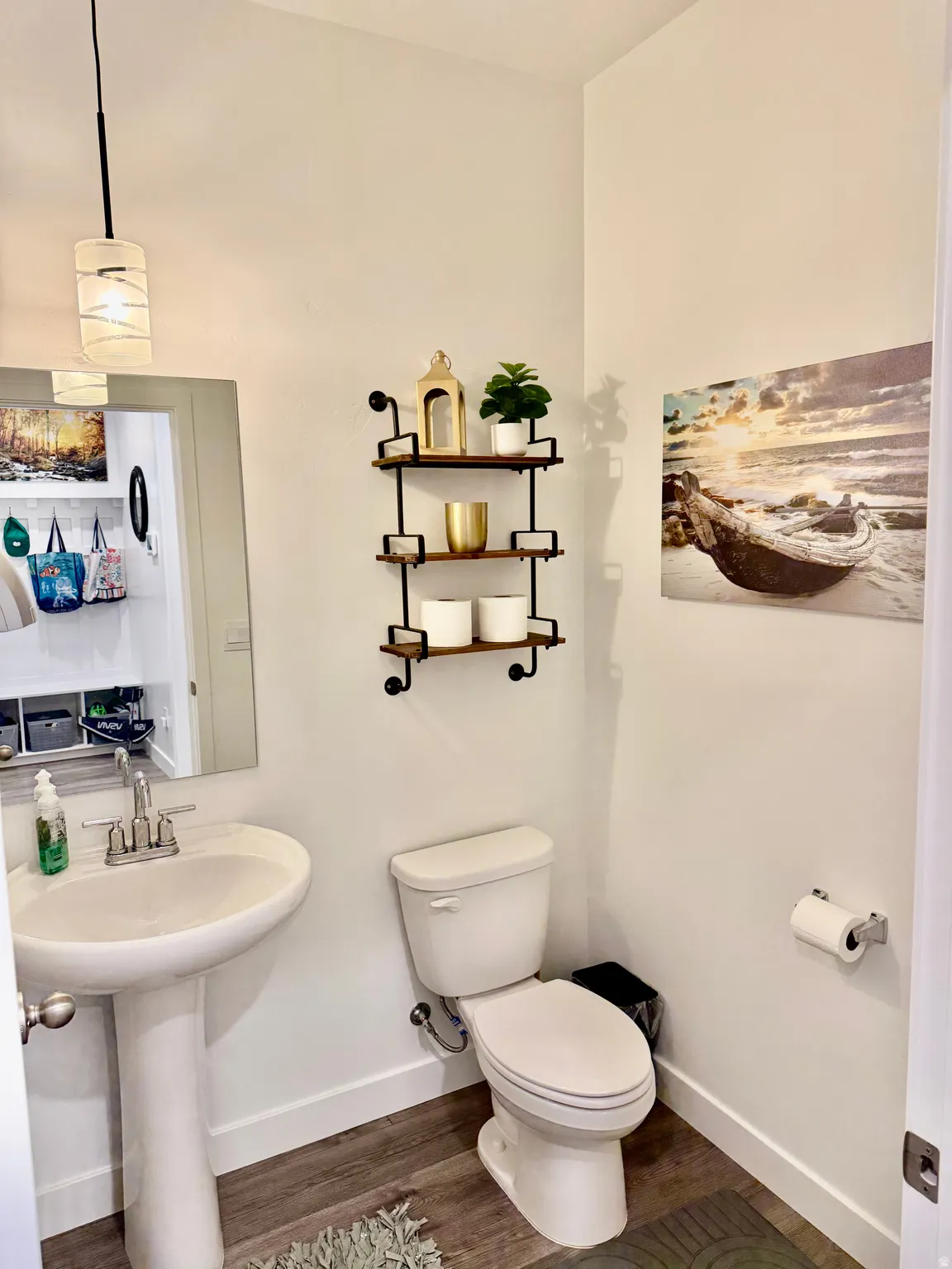 Pedestal sink with chrome-finish faucet, toilet, wood-finish flooring, and wall-mounted shelving
