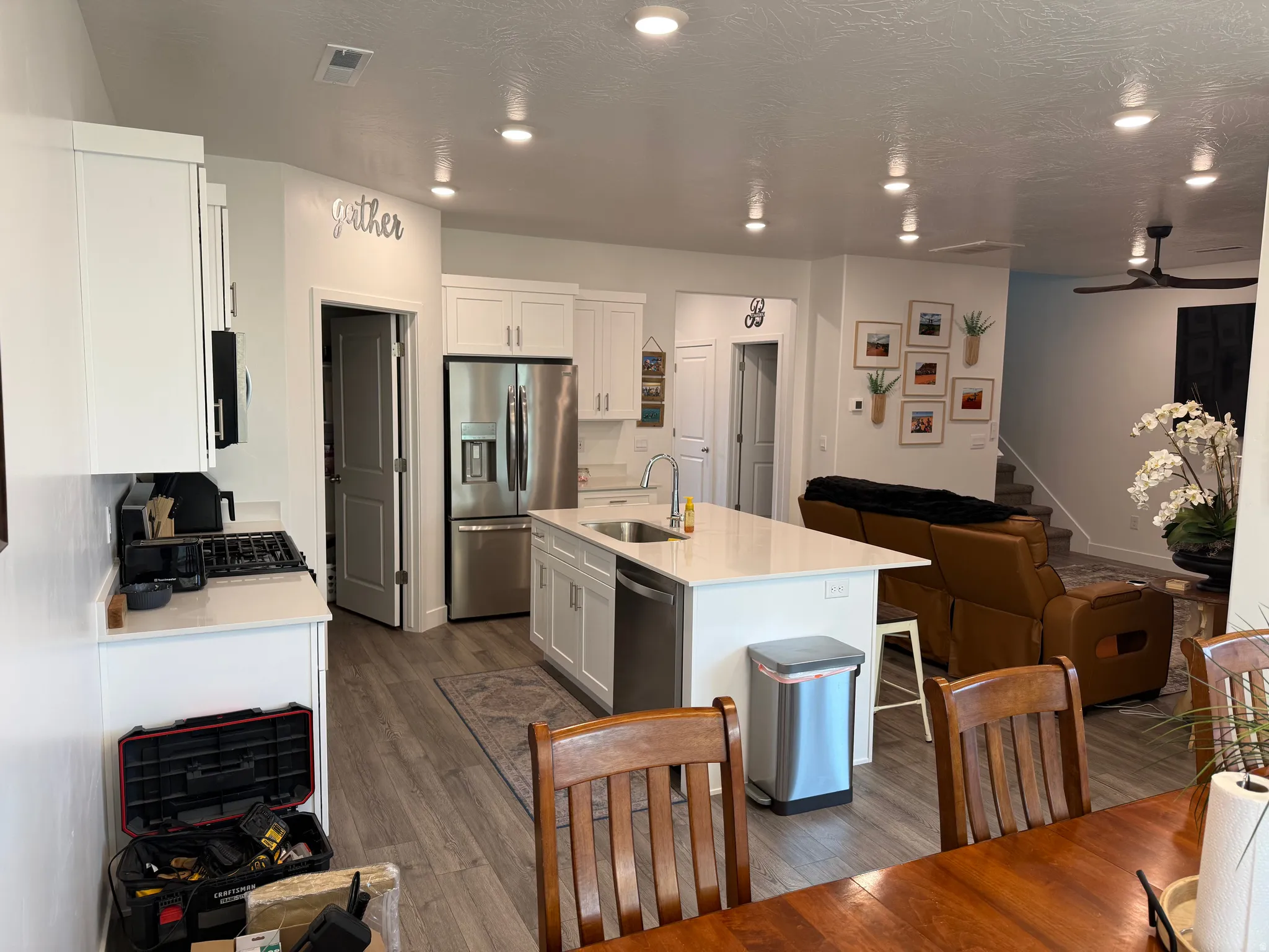 Open-concept kitchen featuring an island with sink, white cabinetry, stainless steel appliances, and wood-finish flooring
