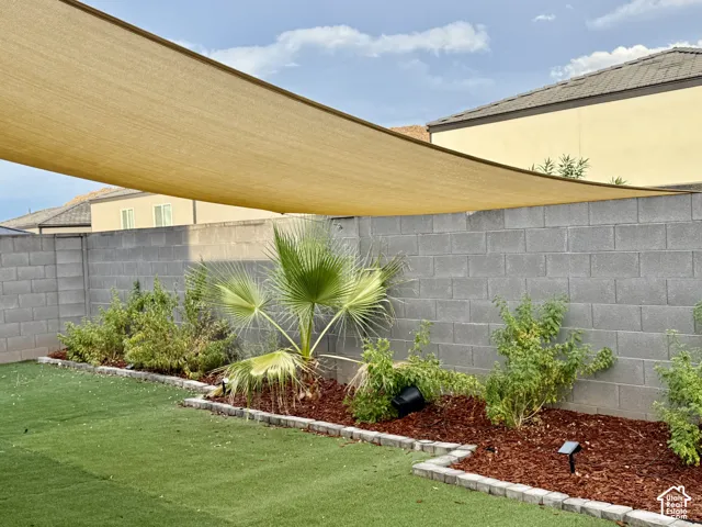 Expansive backyard featuring artificial turf, a shade sail, and landscaped planting beds with decorative wood chips and assorted foliage