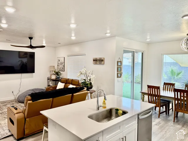 Open-concept living area featuring a kitchen island with sink, stainless steel dishwasher, sliding glass door access to the outdoor space, and wood-finish flooring