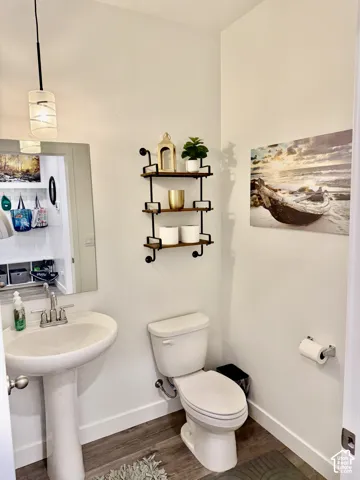 Pedestal sink with chrome-finish faucet, toilet, wood-finish flooring, and wall-mounted shelving