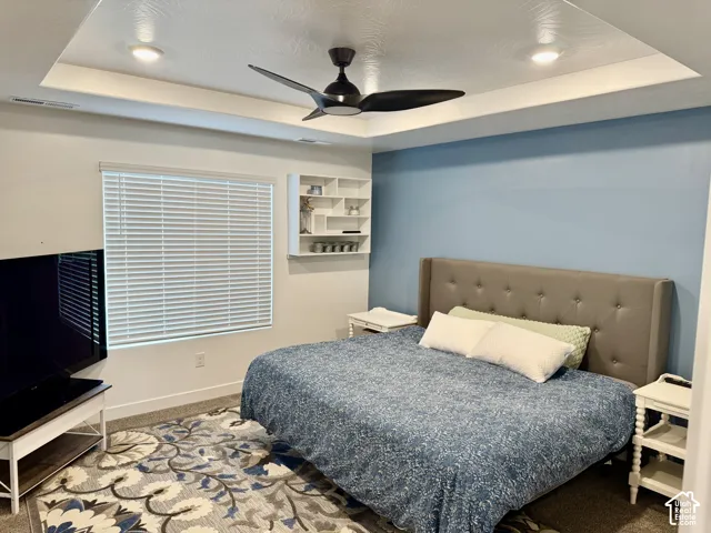 Tray ceiling with recessed lighting, ceiling fan, window with blinds, and built-in shelving