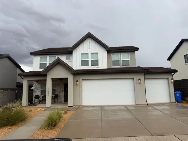 Two-story facade with stucco and vertical white siding accents, covered entry porch, multiple windows with white trim, attached two-car garage, and a single-car garage