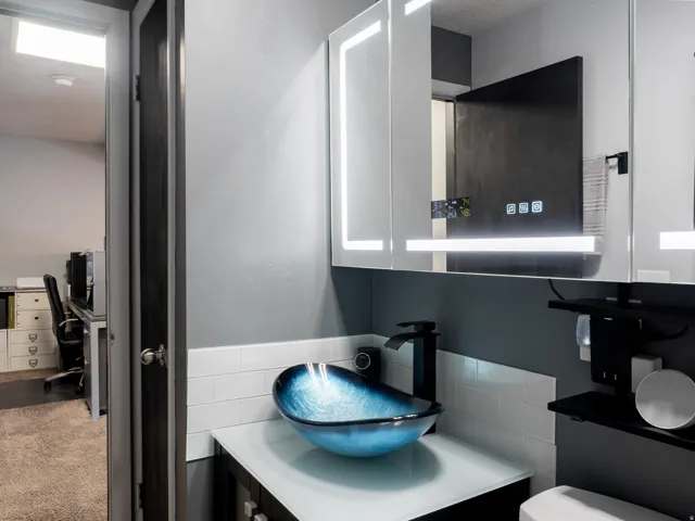 Custom vessel sink with a black finish faucet, paired with illuminated medicine cabinets
