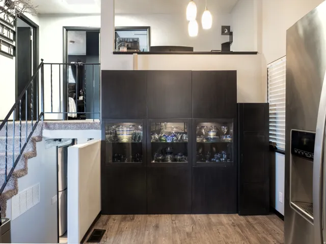 Wood-finish flooring, built-in display cabinetry, stainless steel refrigerator, carpeted staircase with metal railing, and pendant lighting fixtures