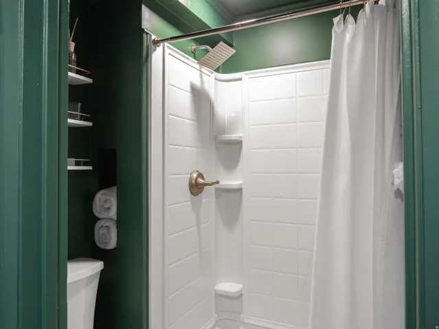 White shower enclosure with integrated shelving, rainfall shower head, and bronze-finish shower controls