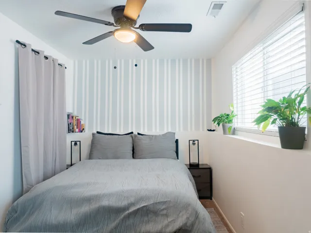 Window with blinds, striped accent wall, ceiling fan with integrated lighting, wall-mounted shelving