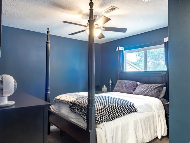 Ceiling fan with integrated lighting, window with white trim, dark wall paint, textured ceiling, dark wood-finish bed frame