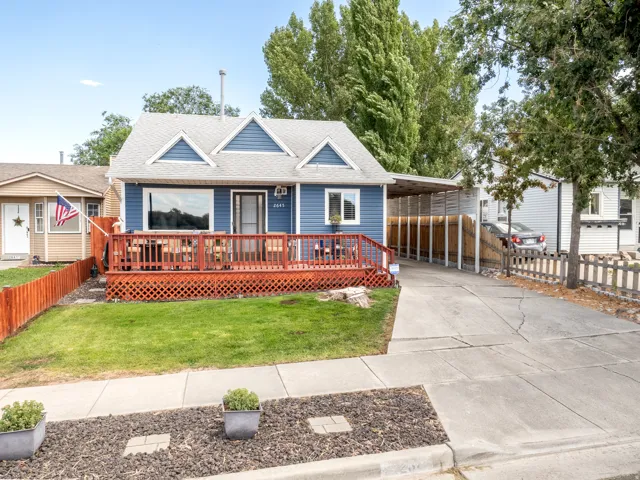 Blue siding exterior with three prominent gables, a red-stained wood deck, a covered carport, and a concrete driveway