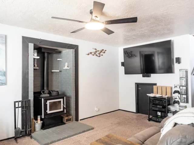 Living area featuring a ceiling fan, wood-burning stove with brick surround, and a wall-mounted television