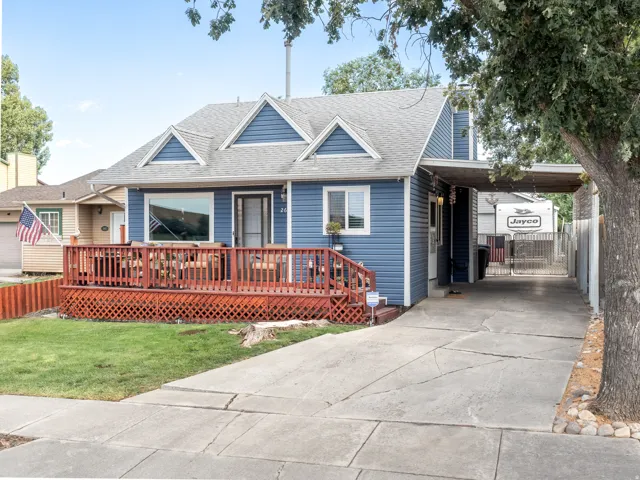 Blue vinyl siding, a gabled roofline, an expansive wood-finish deck, a concrete driveway, and an attached carport