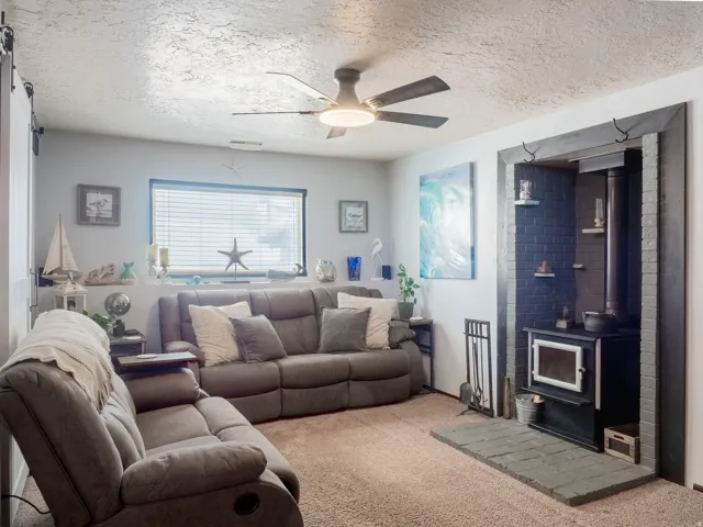 Wood-burning stove set within a black brick surround and hearth, featuring an integrated ceiling fan, and a large window with blinds